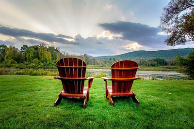 Adirondack chairs on a patch of green grass facing the mountains