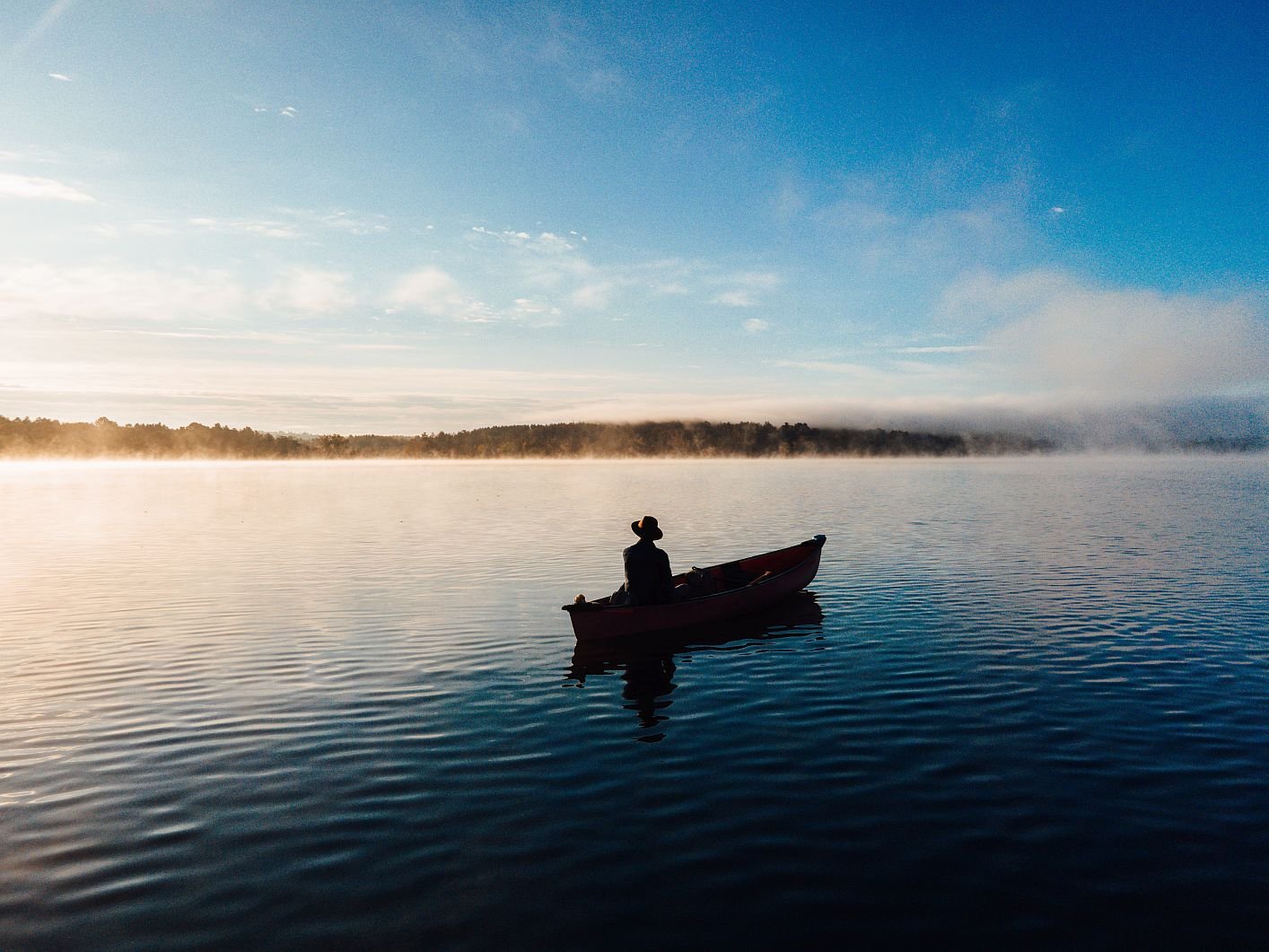 Solo angler in a rowboat on a calm misty Berkshires lake at sunrise