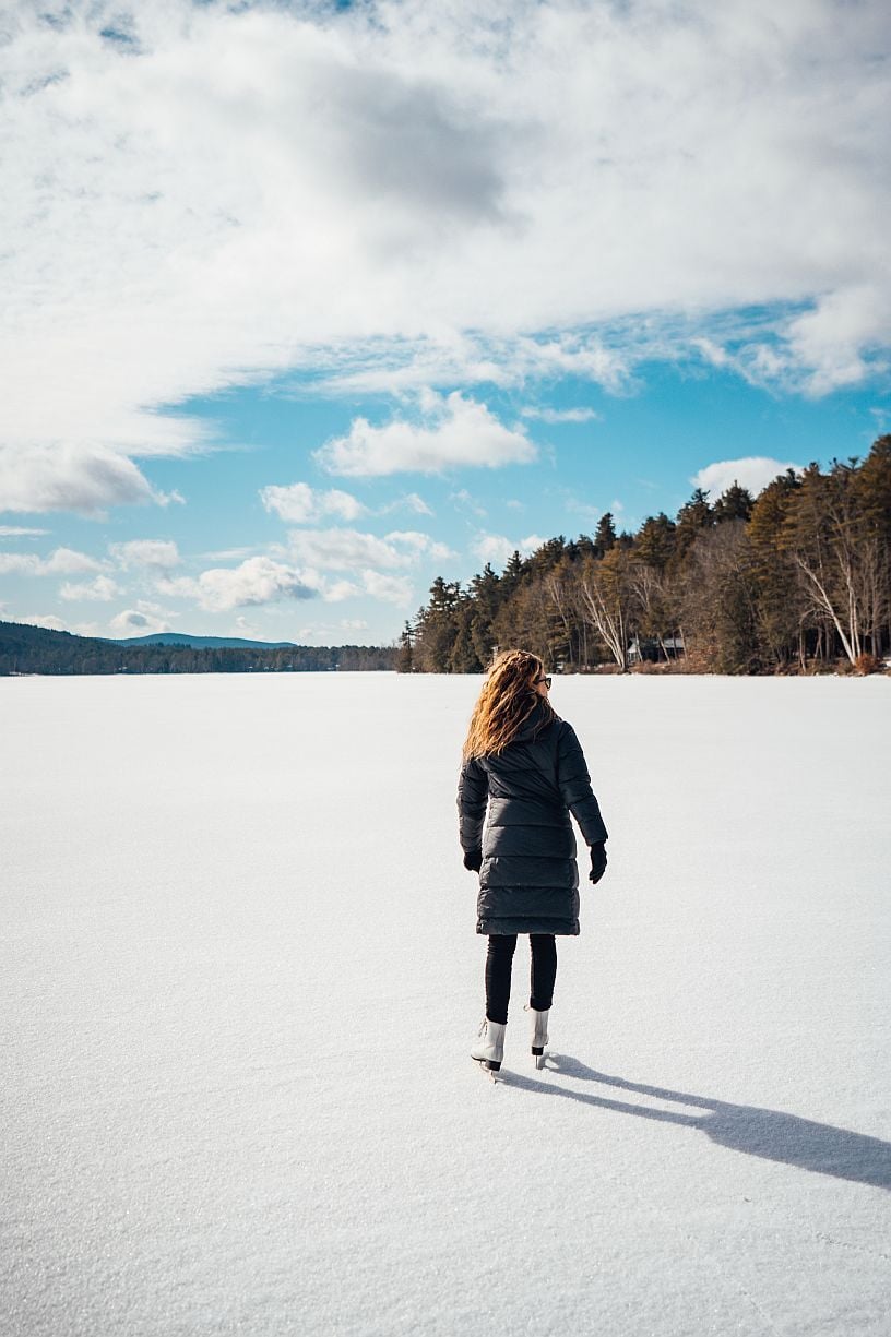 Person standing at the shore of a Berkshires lake taking in views of the surrounding wooded hills