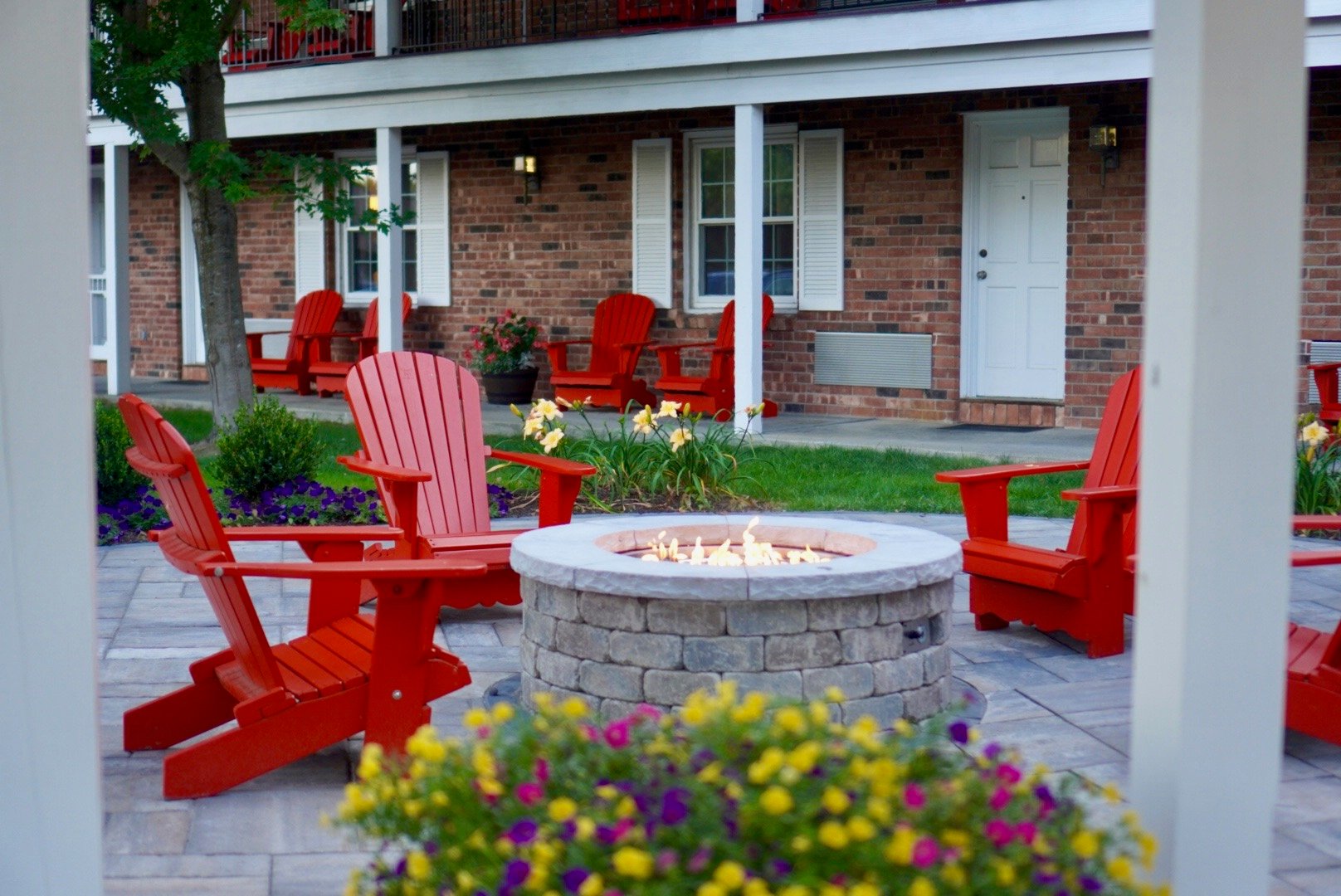 Red Adirondack chairs around a lit fire pit surrounded by spring flowers at The Yankee Inn