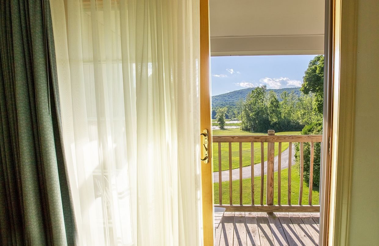 Sheer curtains framing a private balcony with wooden railing overlooking the rolling Berkshire mountains at The Yankee Inn