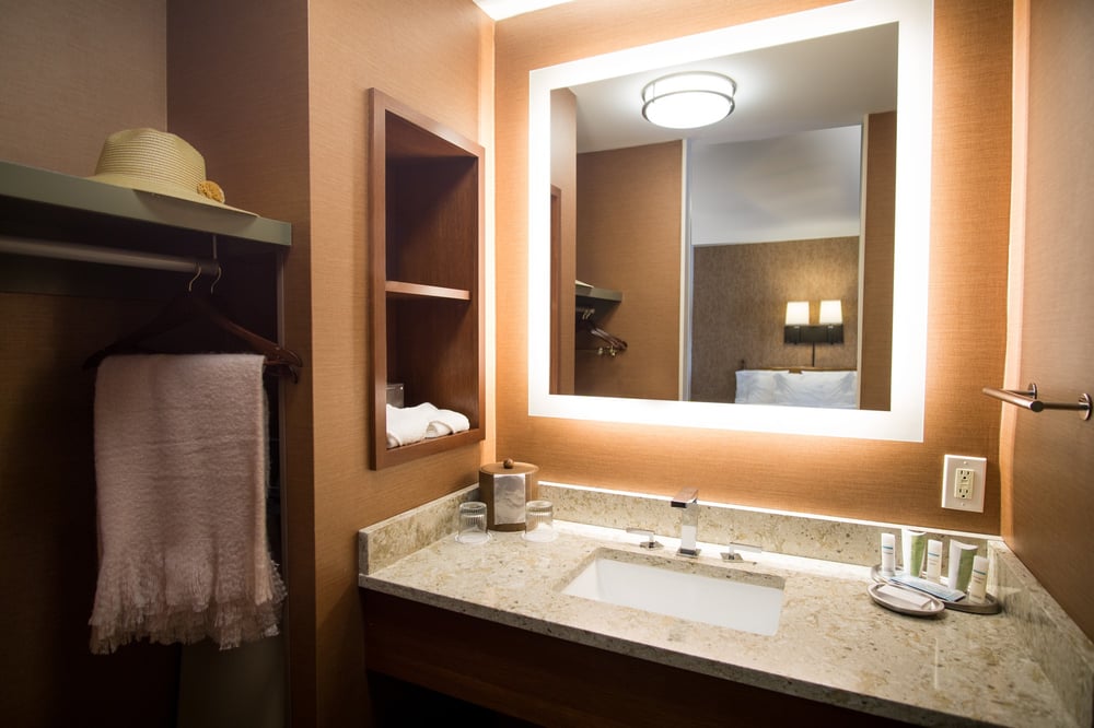 Modern guest bathroom with backlit LED vanity mirror, stone countertop, walk-in closet, and complimentary toiletries