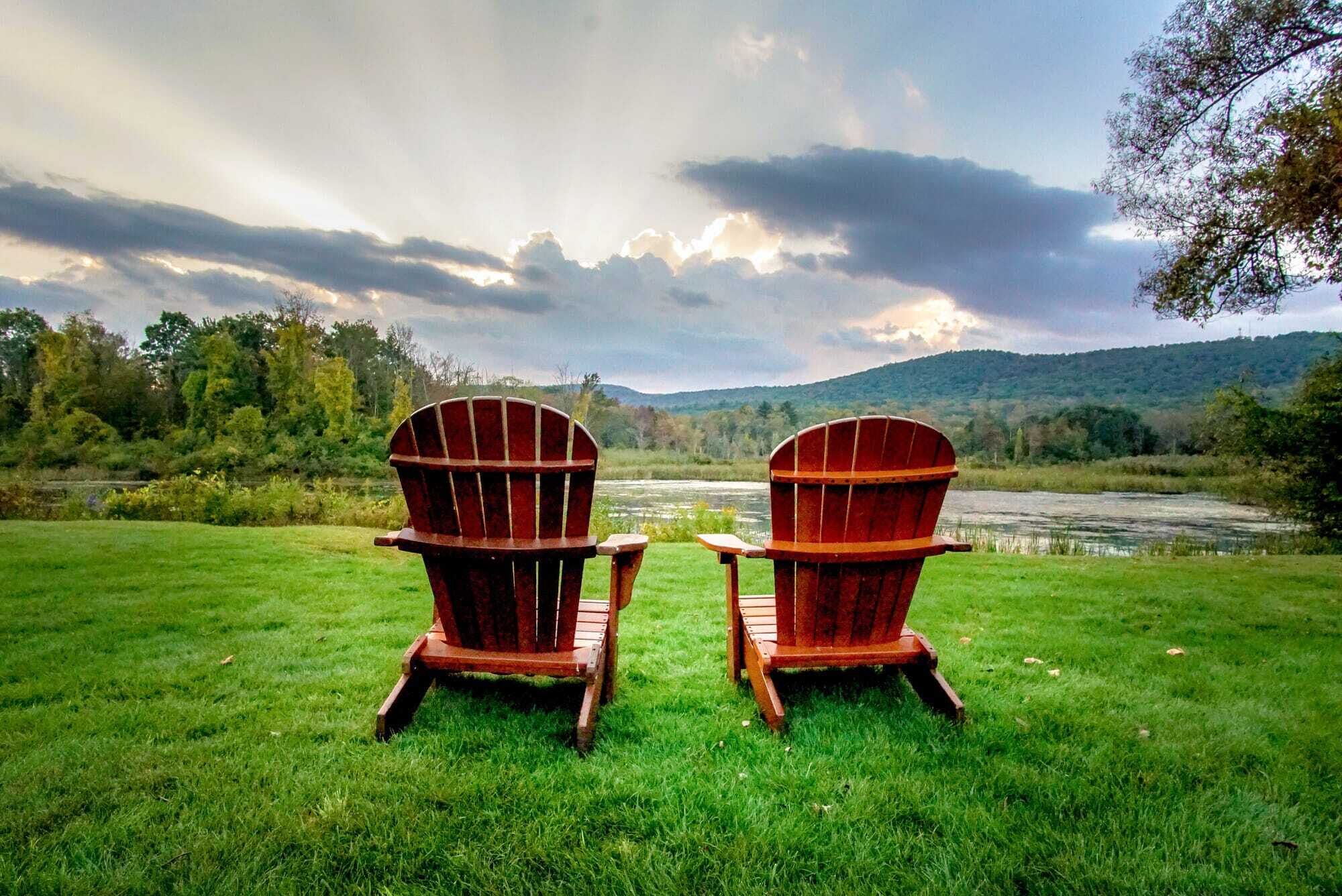 Two wooden Adirondack chairs facing a Berkshires pond and mountain view at sunset