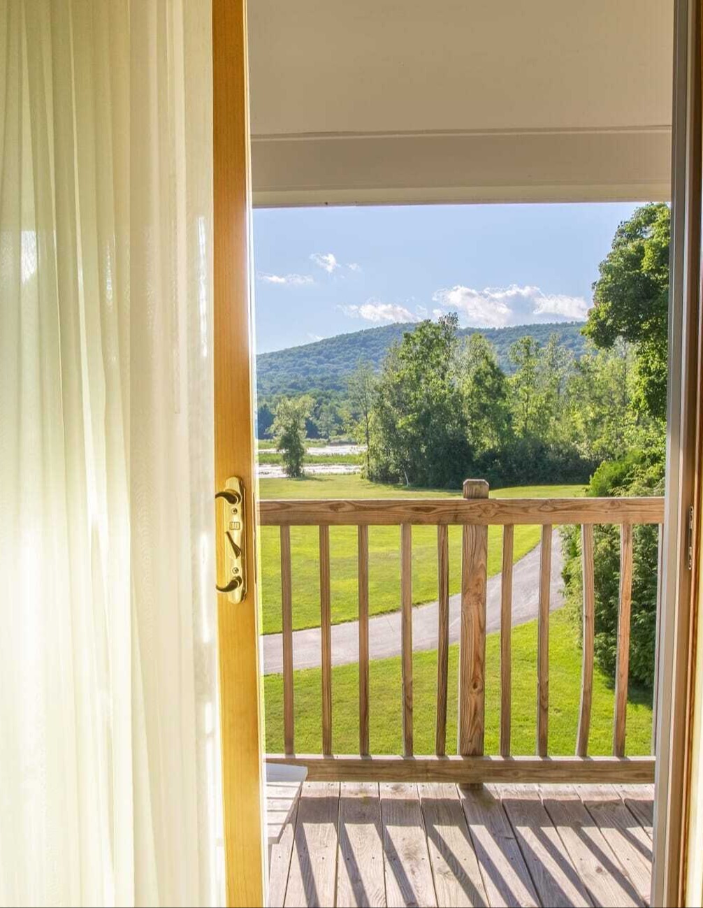 Sheer curtains framing a private balcony with wooden railing overlooking the rolling Berkshire mountains at The Yankee Inn
