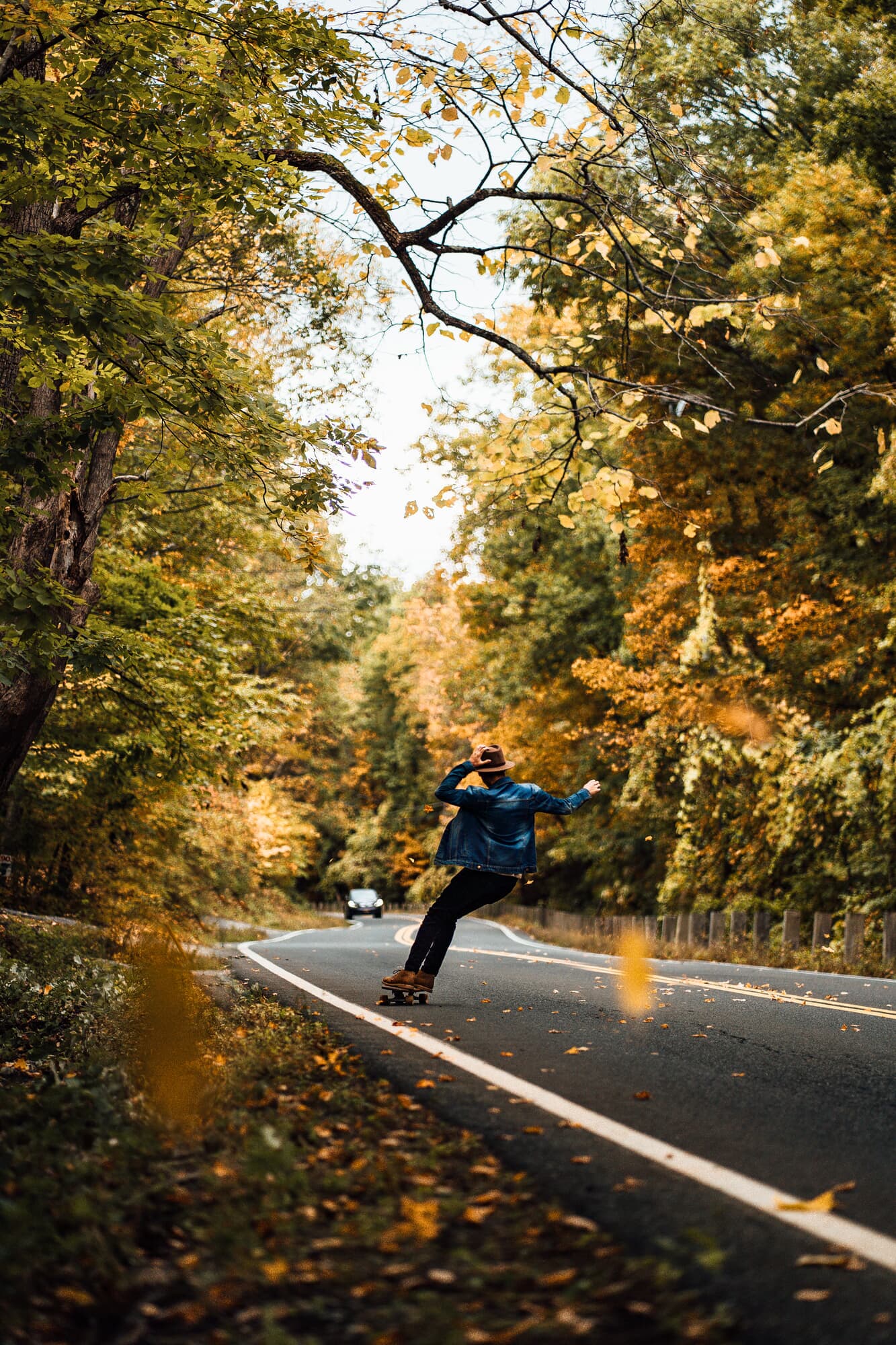 Skateboarder cruising down a tree-lined road framed by golden fall foliage in the Berkshires