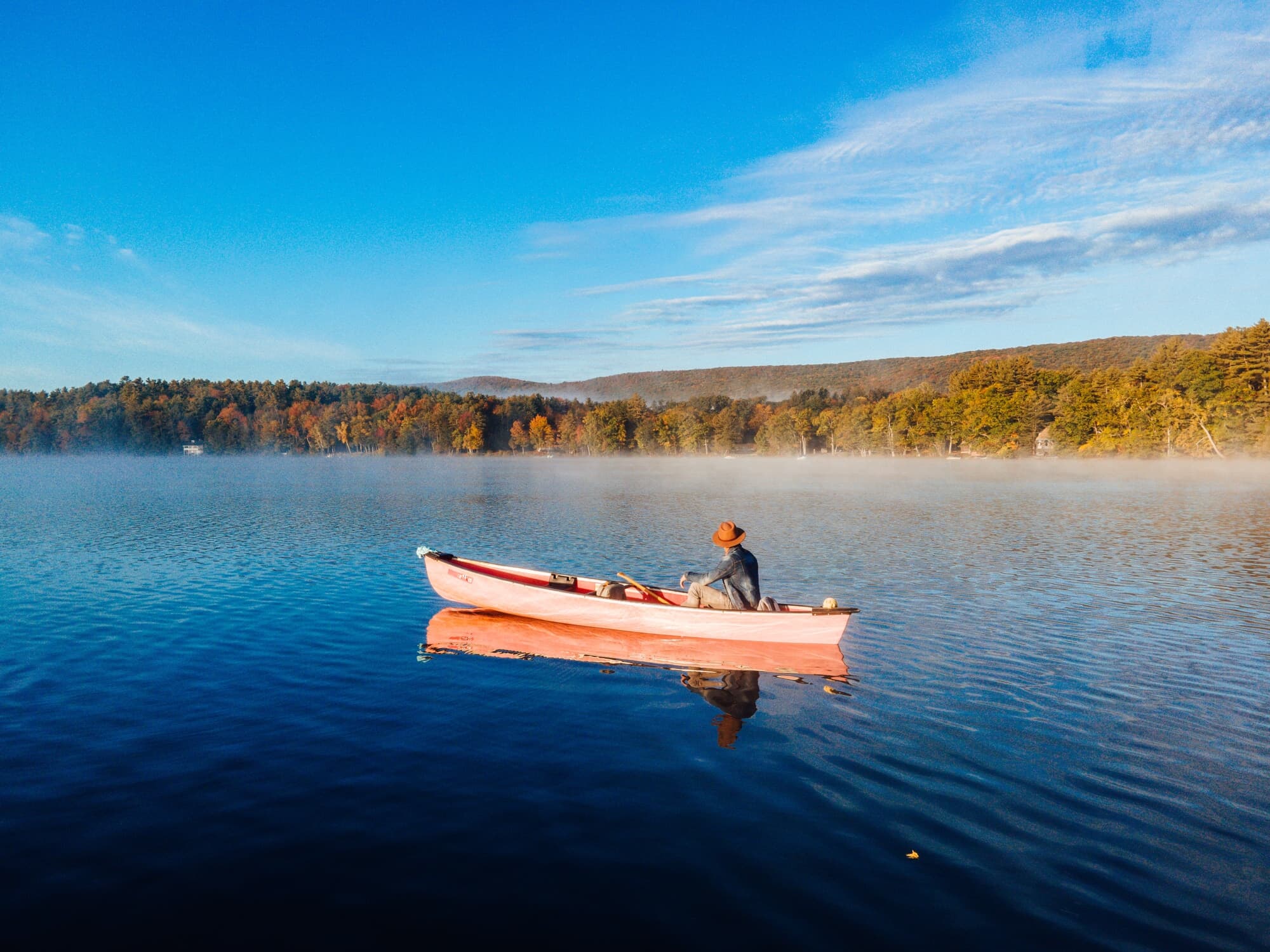 Solo rower on a misty Berkshires lake at sunrise with fall foliage along the shoreline