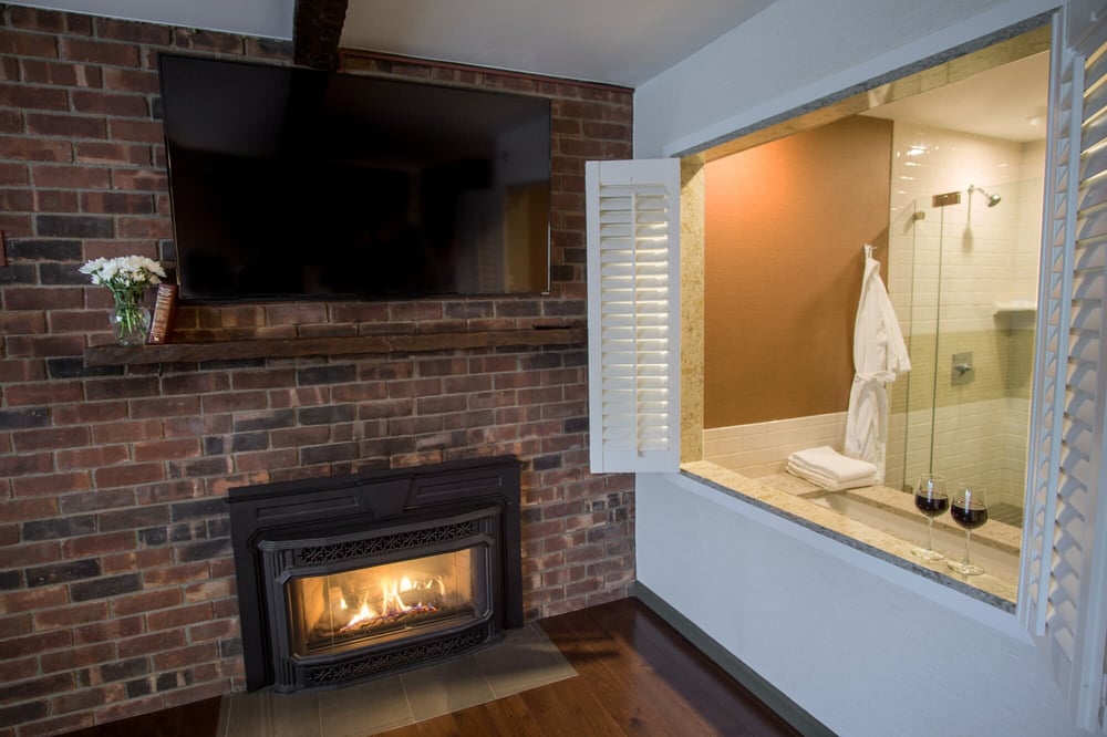 Gas fireplace with exposed brick surround, mounted TV, and walk-in shower viewing window in the King Premier Room