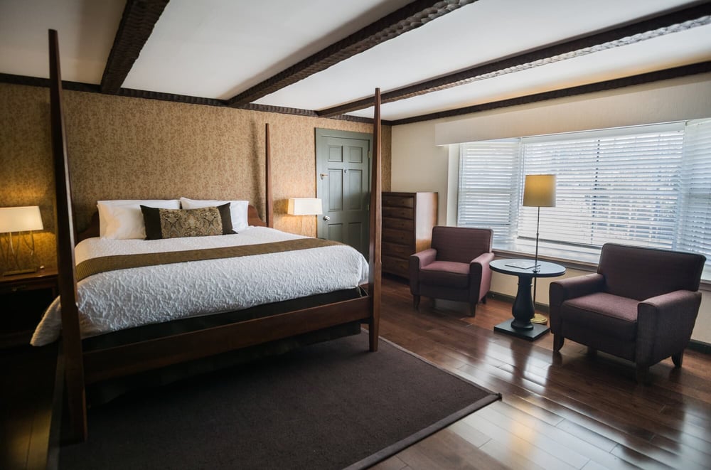 Spacious King Premier Room with four-poster bed, wood-beam ceiling, and private sitting area with armchairs