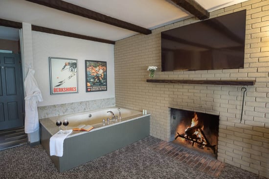 In-room jetted tub beside a brick wood-burning fireplace with mounted TV in the King Superior Room at The Yankee Inn