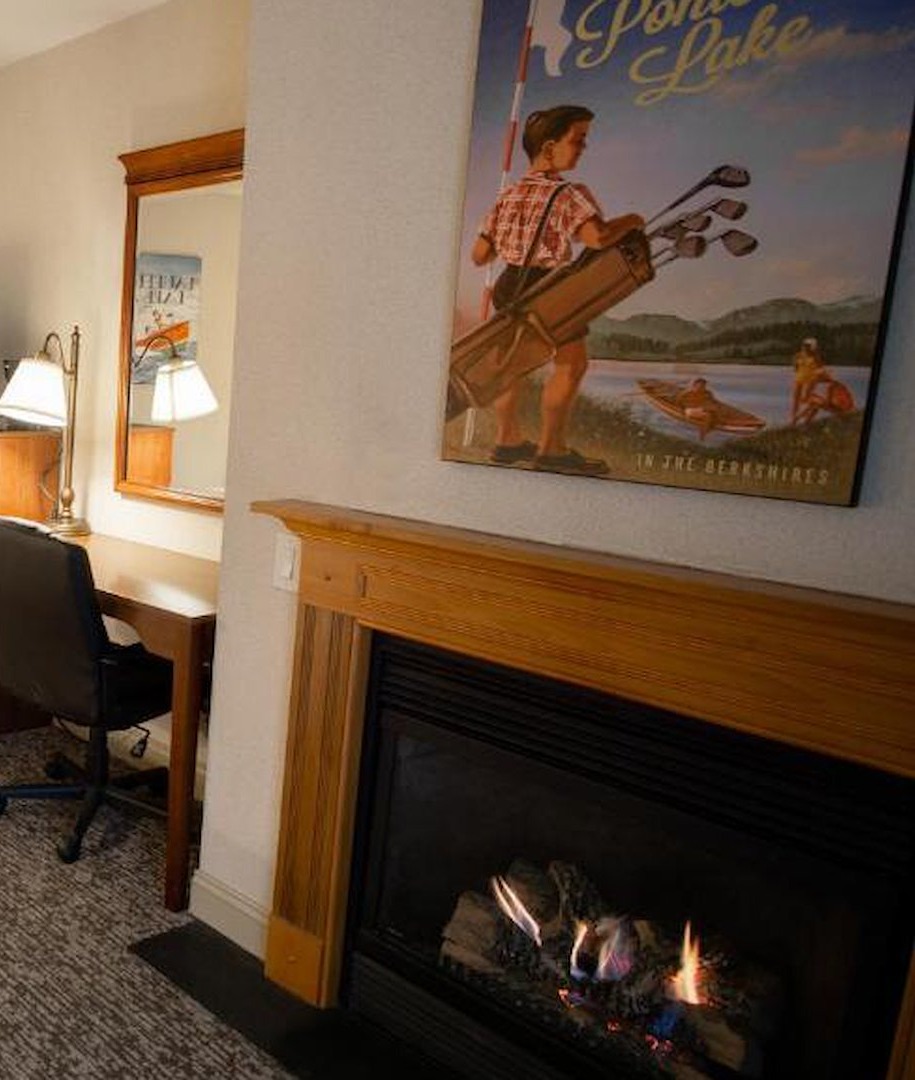 In-room gas fireplace beside a sitting area with vintage Berkshires lake artwork