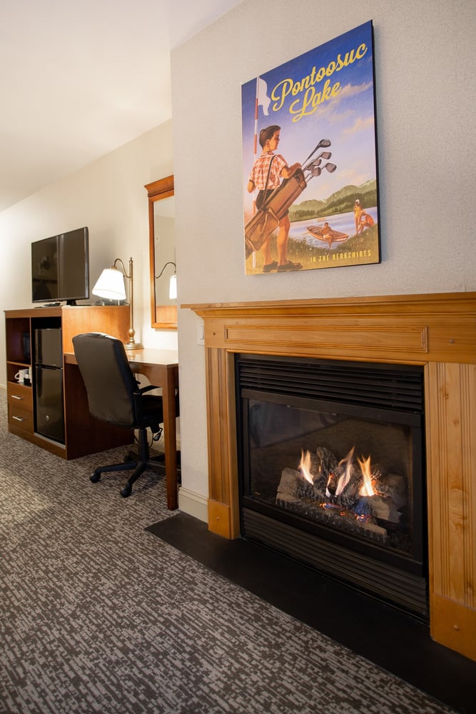 Gas fireplace with wooden mantel and adjacent work desk with mini-fridge in the King Deluxe Room