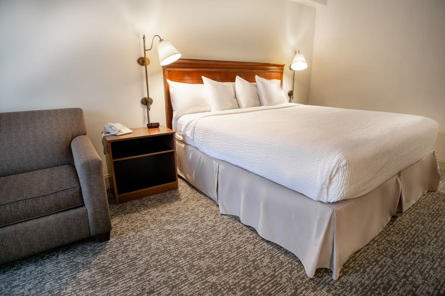 King bed with wooden headboard, plush white linens, and an upholstered armchair in a Deluxe King guest room