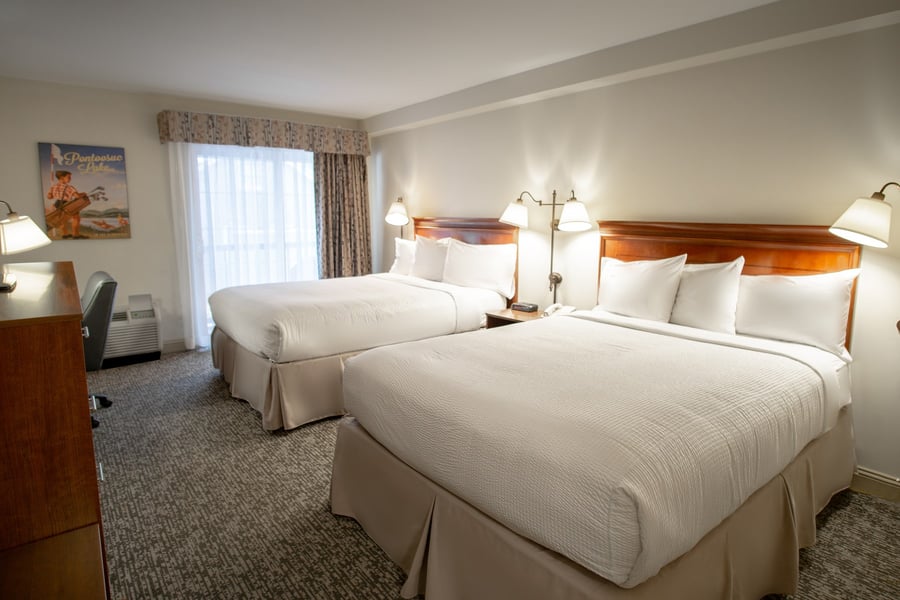 Two queen beds with wooden headboards and crisp white linens beside a sunlit window in a Deluxe Two Queen room