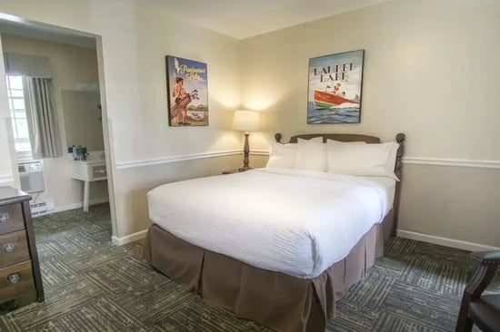Queen bed with white linens flanked by vintage Pontoosuc Lake and Laurel Lake artwork in a South Lodge guest room