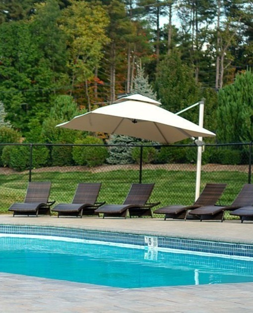 Outdoor pool surrounded by lounge chairs, a large patio umbrella, and lush Berkshires landscaping at The Yankee Inn