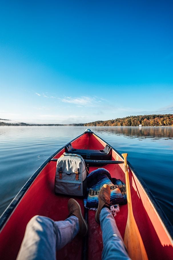 First-person view from a red canoe gliding across a calm Berkshires lake under a clear blue sky