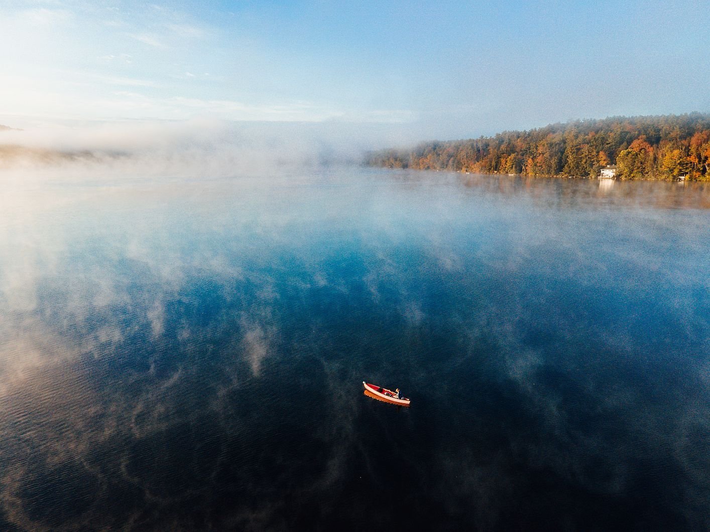 Lone kayaker on calm reflective water with autumn shoreline in the Berkshires