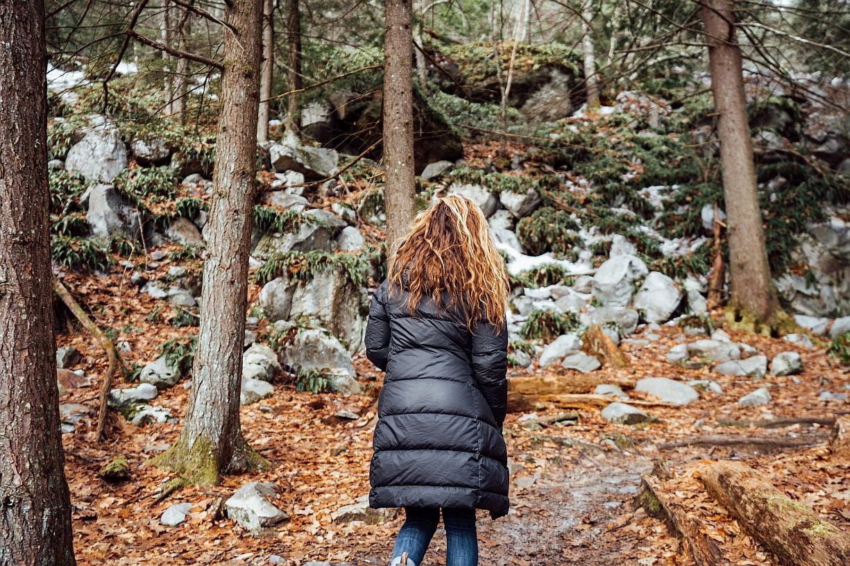 Woman hiking through a rocky snow-dusted forest trail in the Berkshires in late autumn