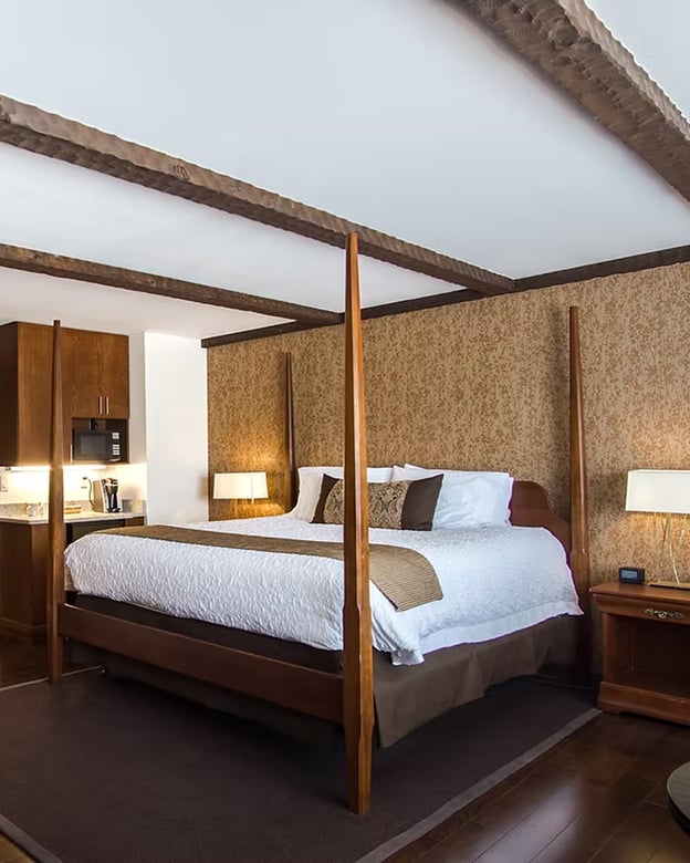 Four-poster king bed beneath rustic wood-beam ceiling in the King Premier Room