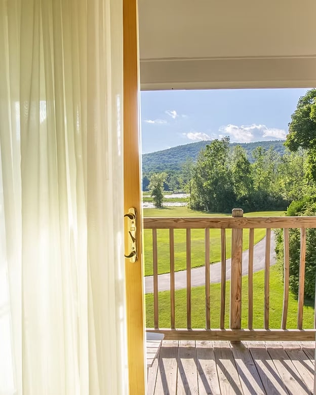 Open balcony door with sheer curtains framing a Berkshire mountain and meadow view from a guest room